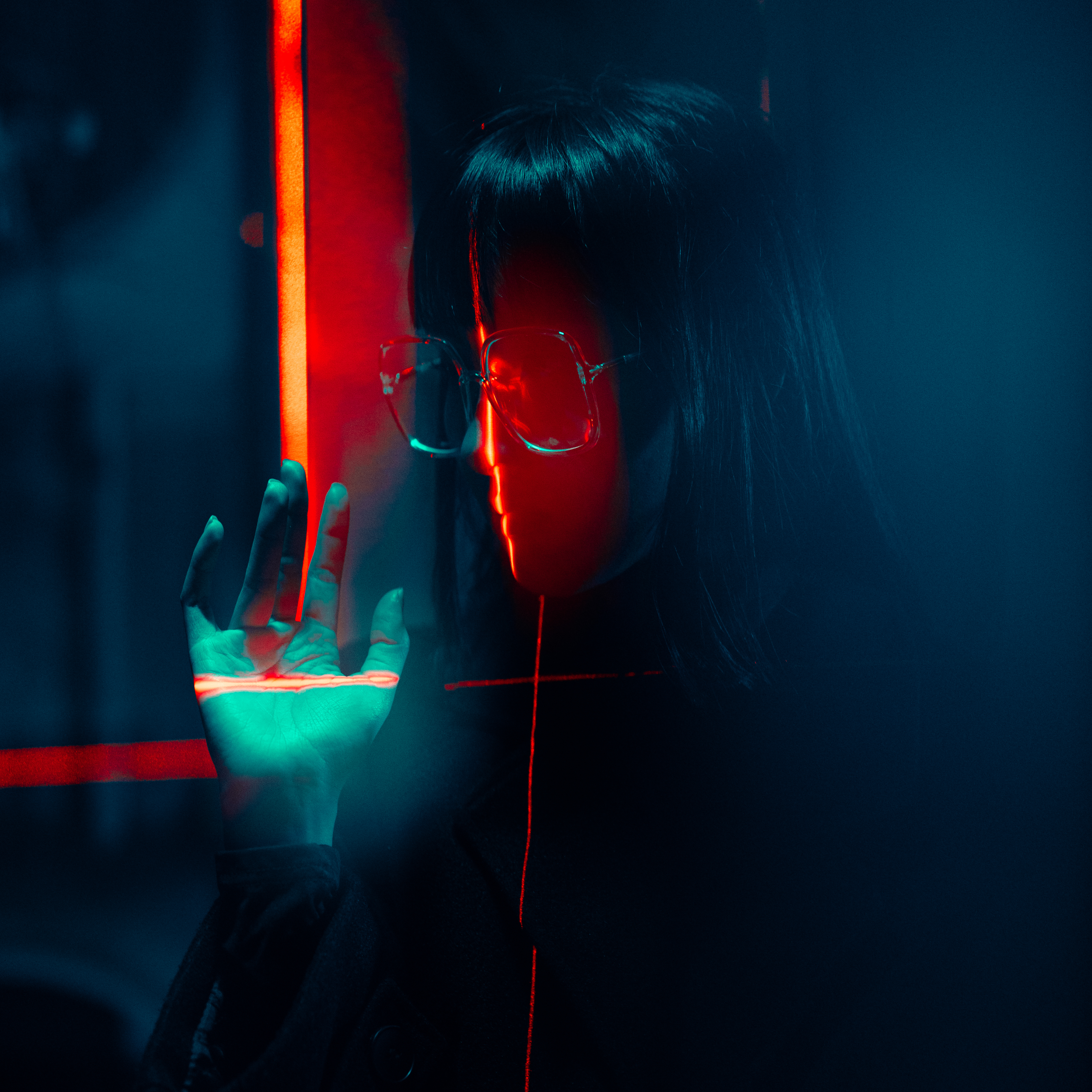 Left side profile of girl looking downwards and right hand raised, with face shrouded by laser lights